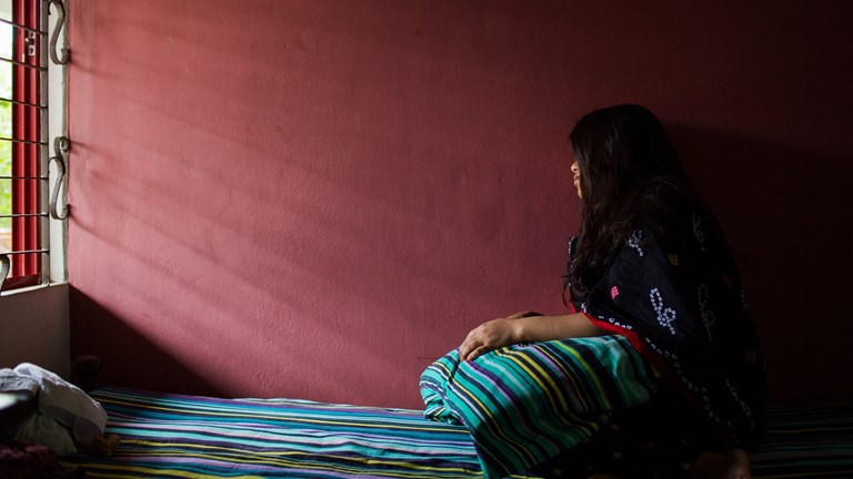 Flicka sitter på säng mot mörkröd vägg